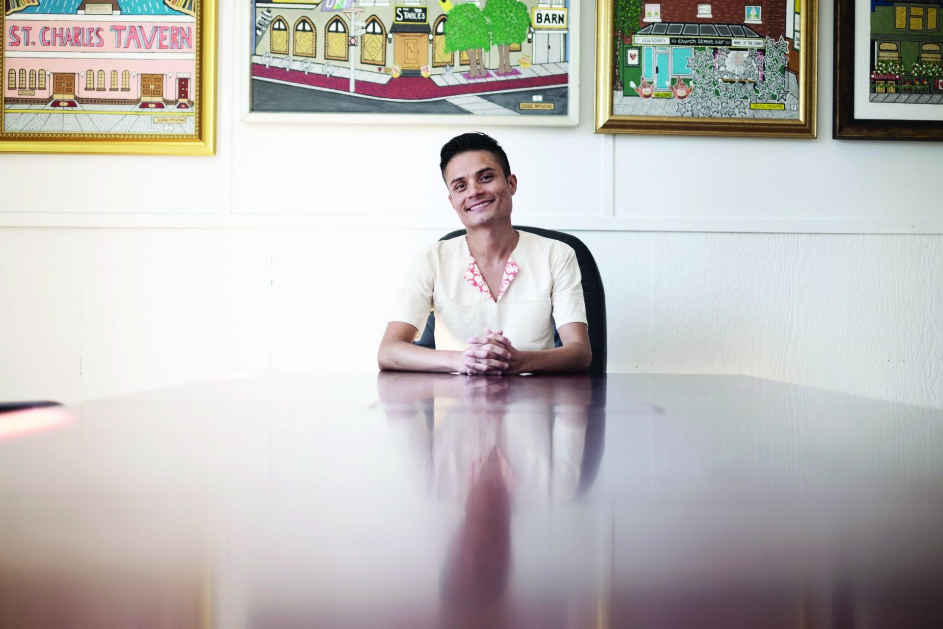 Luis sitting at the top of a table. He is using the shirt made at Sew-what that is cream colored, with a floral print on the inside of the neck area.