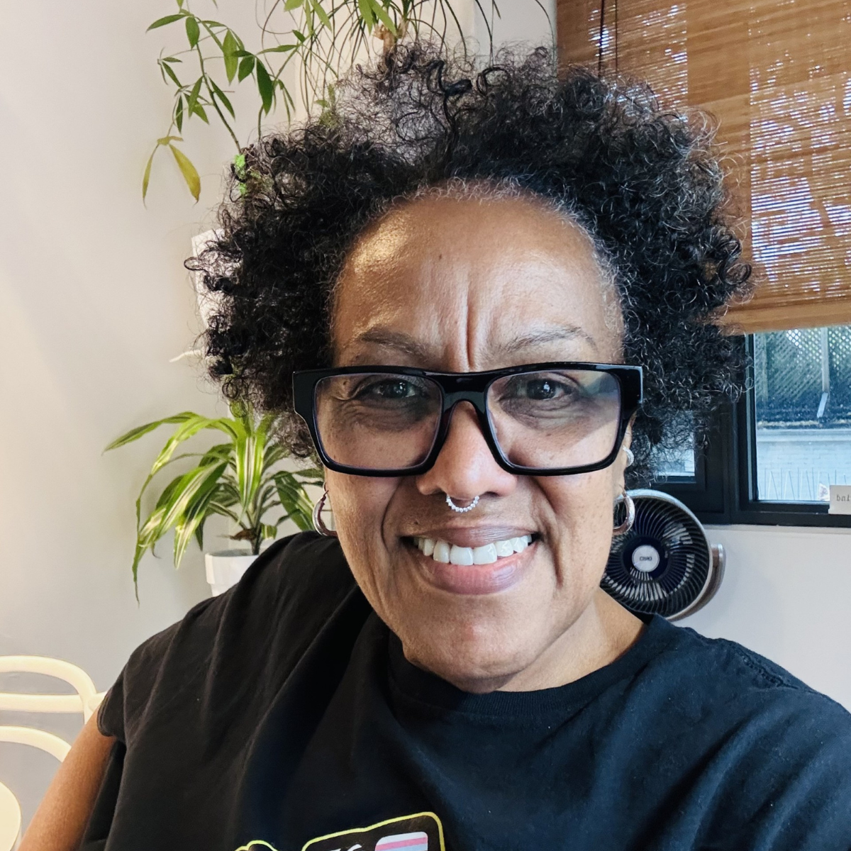 Lisa Duplessis. She is a black woman wearing a blakc t-shirt, black framed glasses and has black curly short hair.