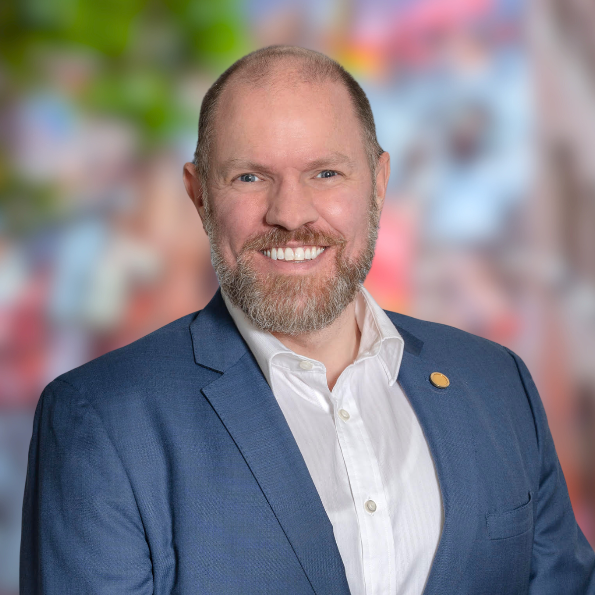 Tom Spence. He is sporting a moustache and beard and is wearing a white shirts and light blue blazer.