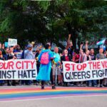 A large group of people holding banners and protesting. Two people on encourage them on bullhorns.