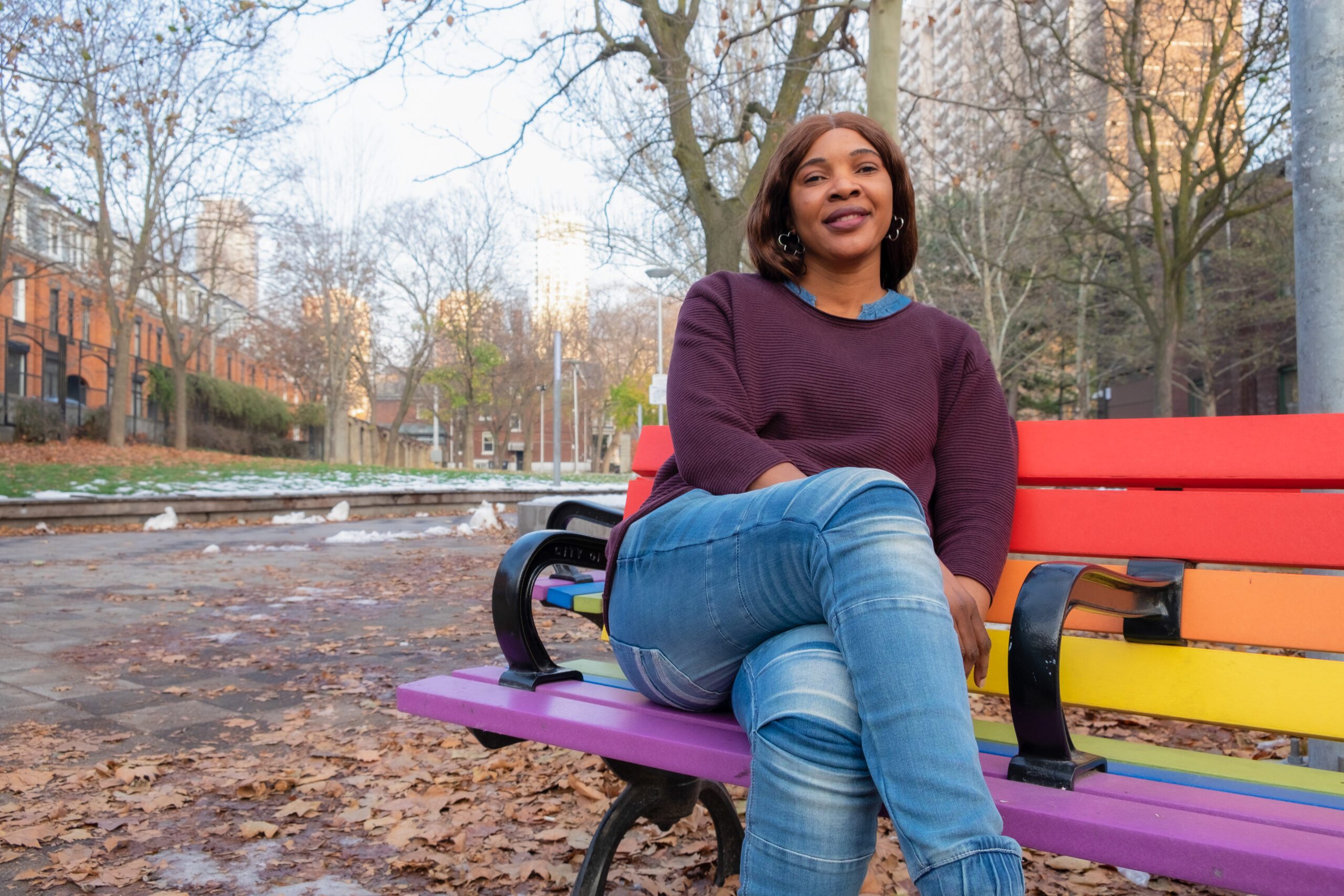 Gloria seated on a park bench coloured in pride flag coloured.